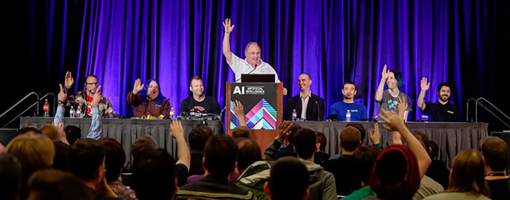 A podium and table with 7 people behind it raising their hand to a crowd of people.